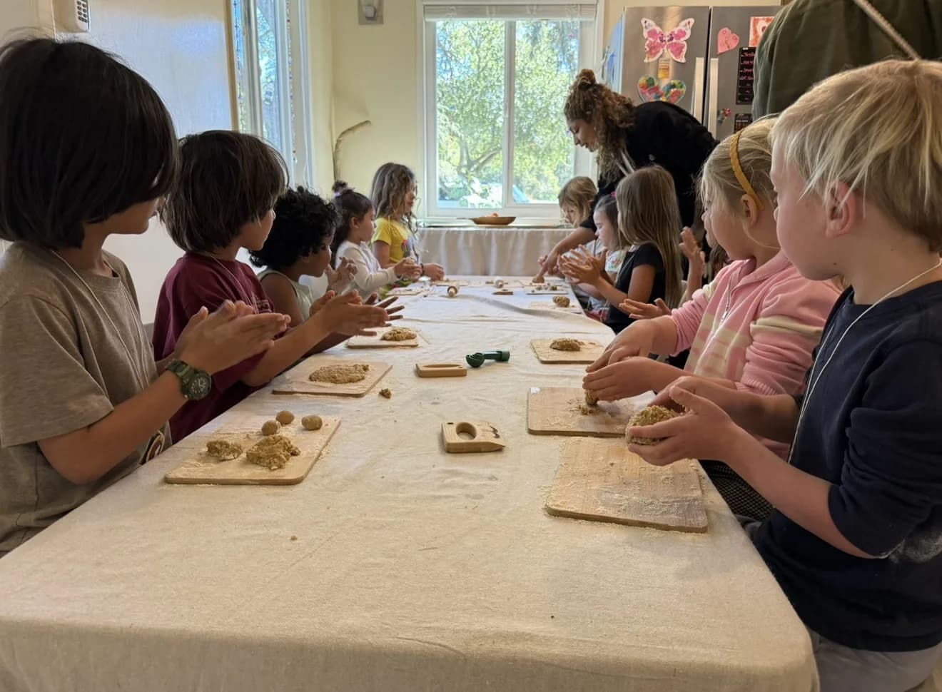 Children shaping natural material together at a long table