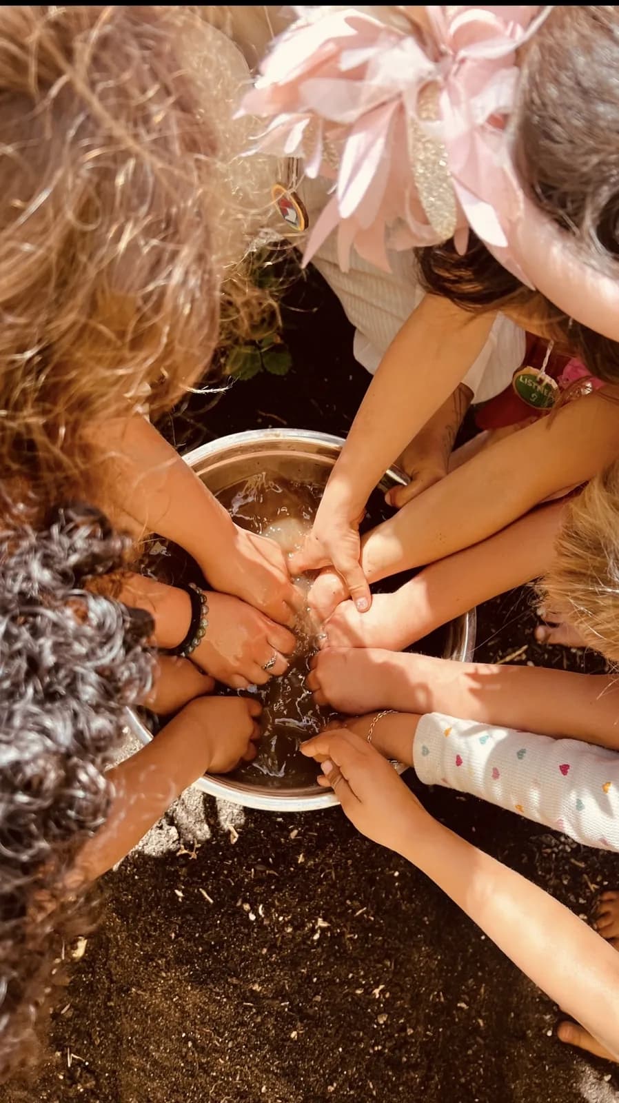 Children gathering their hands around a shared bowl outdoors