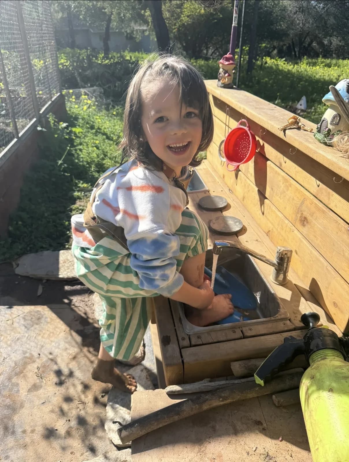 A child washing a doll at an outdoor mud kitchen