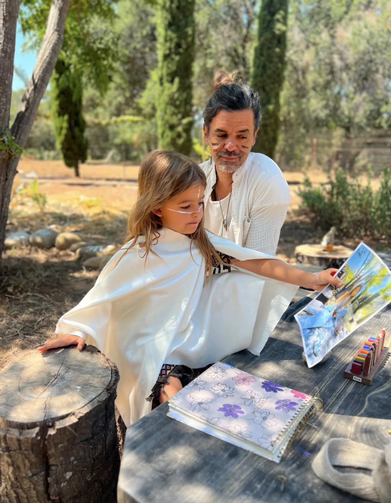 An adult helping a child create art at an outdoor table