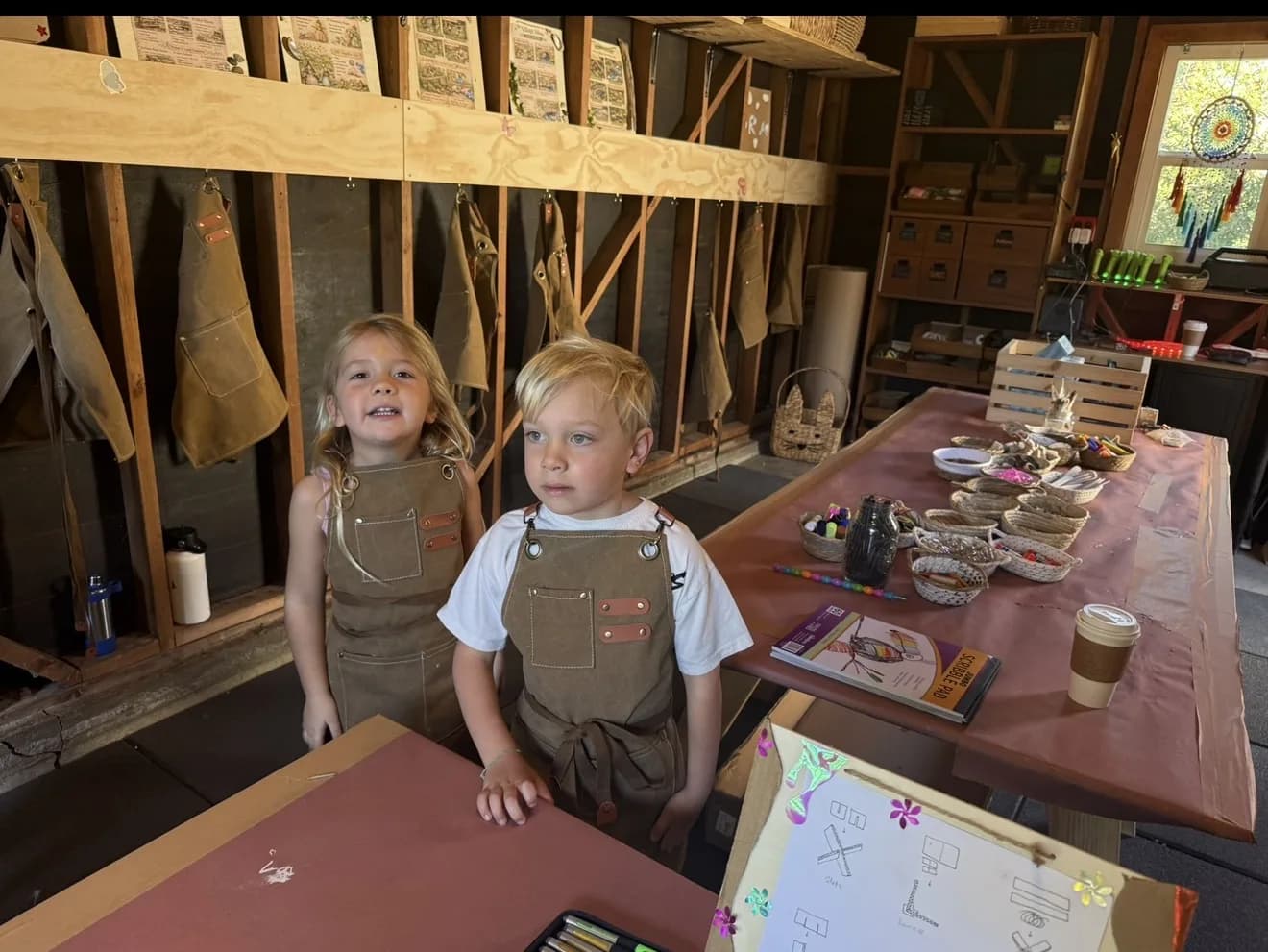 Two young children wearing aprons at a hands-on makers station