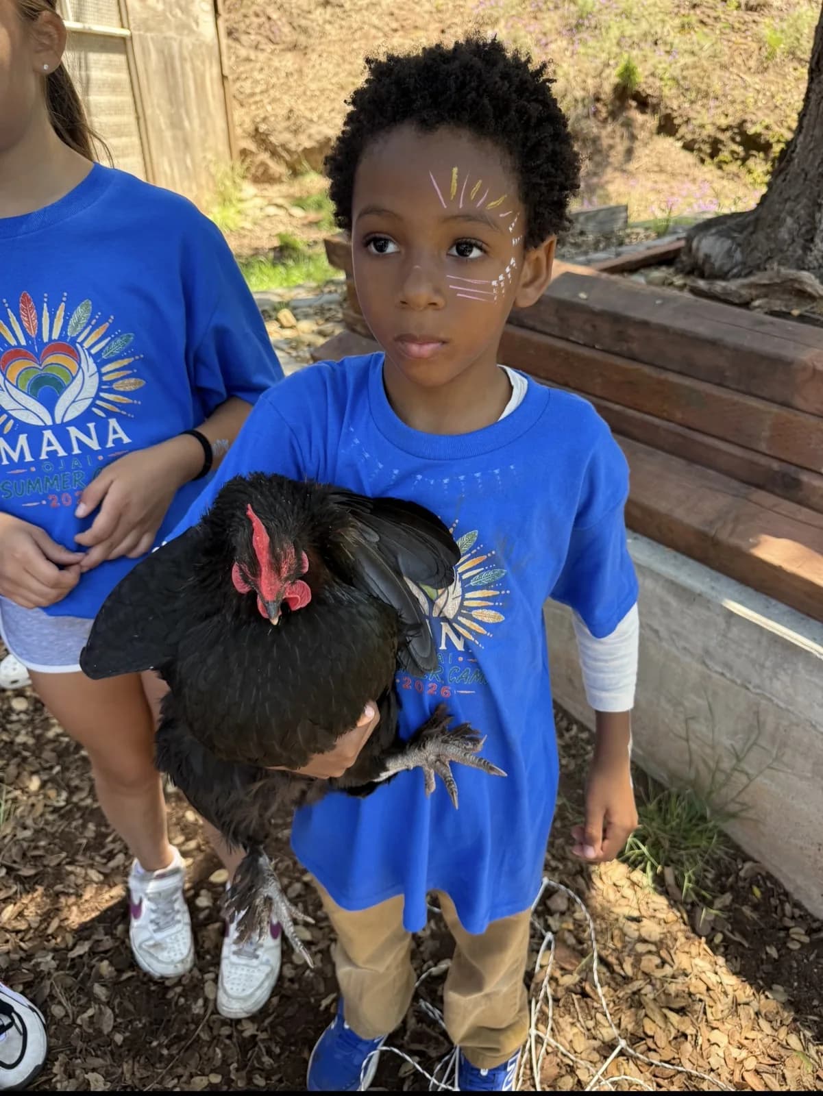 A child in a MANA shirt holding a chicken during an animal-care day