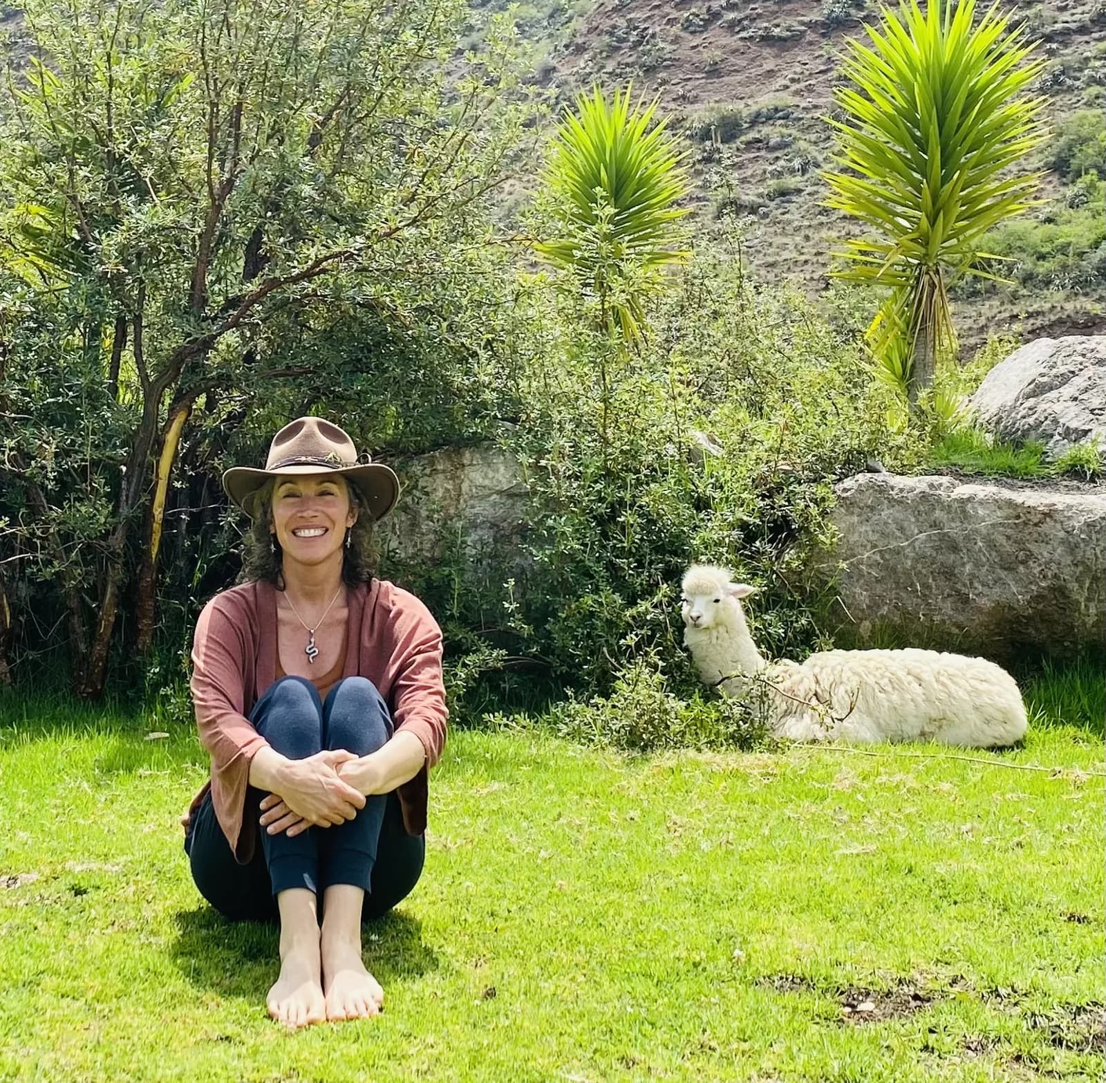 Sonya seated in a mountain garden beside a white alpaca