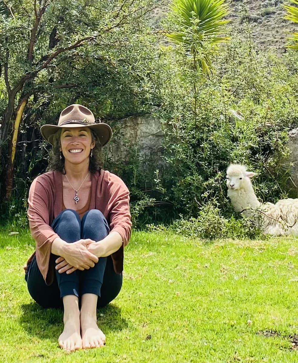 Sonya seated in a mountain garden beside a white alpaca